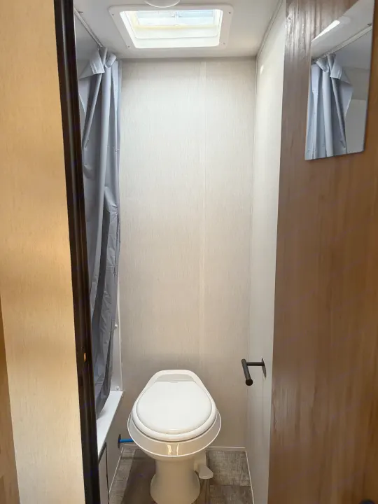 RV rental bathroom: See the compact toilet, shower curtain, and skylight in this efficient space.. Forest River Cherokee Wolf Den 16EV 2024