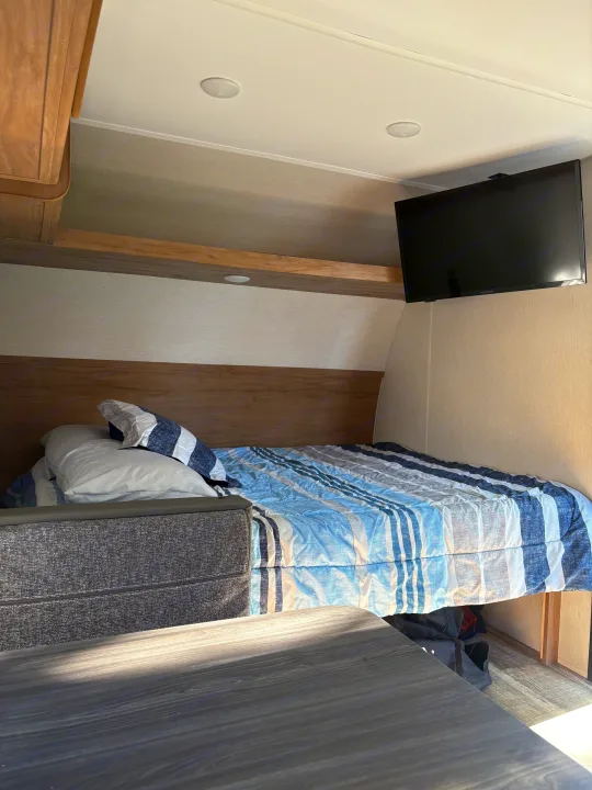Cozy RV rental bedroom features a striped bed, mounted TV, and storage, ideal for travel.. Forest River Cherokee Wolf Den 16EV 2024