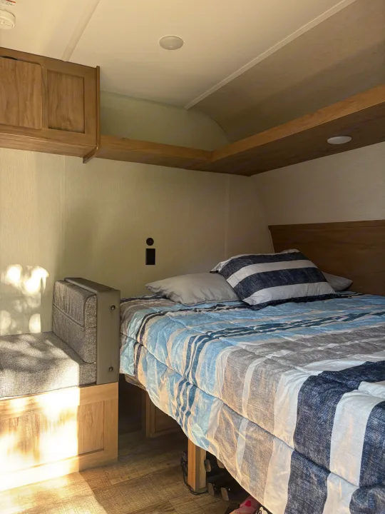 Cozy RV rental bedroom with a striped bed, built-in storage, and bench seating. Ideal for compact travel comfort.. Forest River Cherokee Wolf Den 16EV 2024