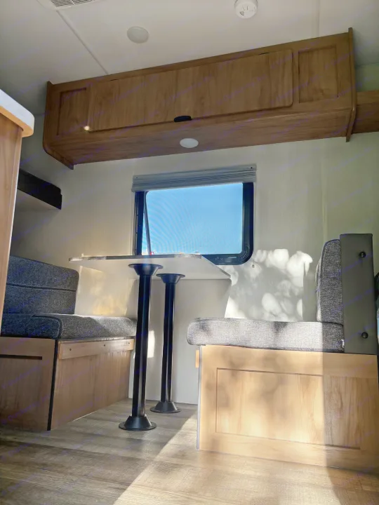 Inside an RV rental, a bright dinette area with built-in bench seating, a table, and sunlight streaming through the window.. Forest River Cherokee Wolf Den 16EV 2024