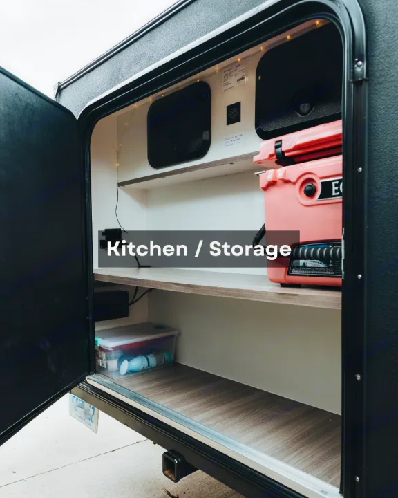 An open RV rental exterior compartment with shelves, a pink cooler, and organized supplies for an outdoor kitchen/storage setup.. Other Other 2022