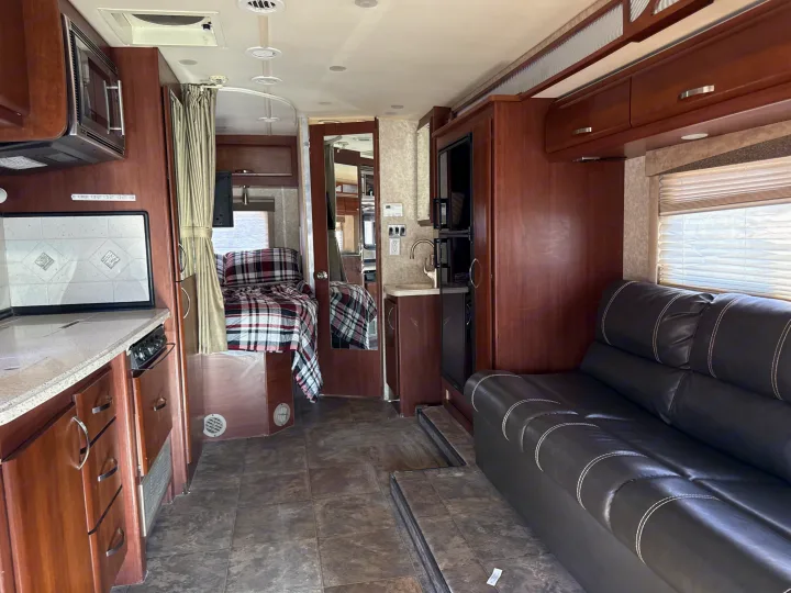 Inside an RV rental: full kitchen, bedroom with plaid bedding, and a black leather sofa. Ready for travel.. Fleetwood Tioga 2011