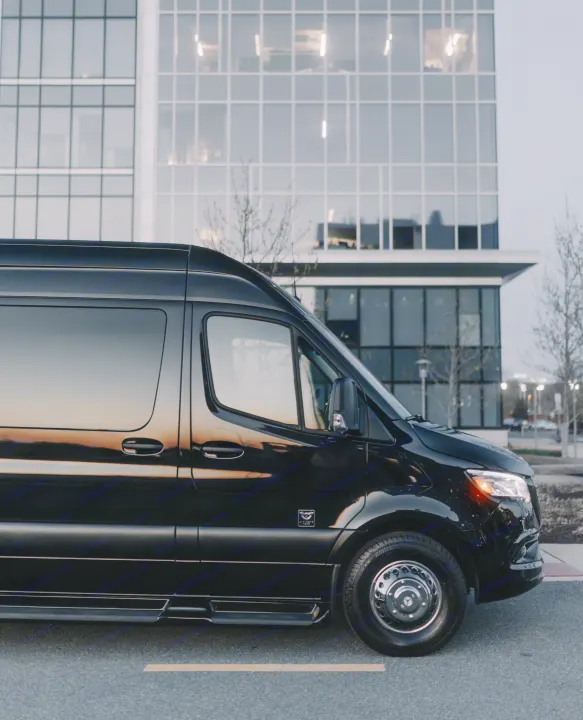 A polished black luxury van, suitable for an RV rental, sits on a street with a large, modern glass building behind it.. Ultimate Toys Ultimate Freedom XL 2025