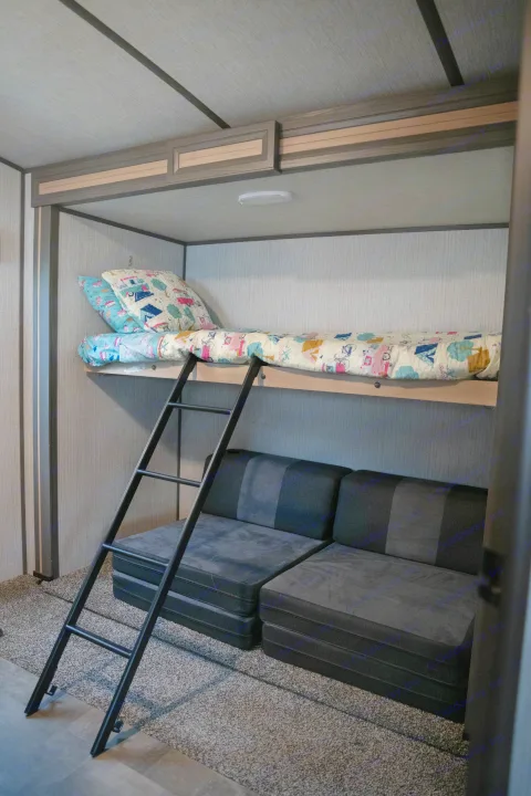 RV rental bunk bed with colorful bedding, a ladder, and dark grey modular seating below for compact sleeping.. Cruiser RV Radiance Ultra Lite 2020