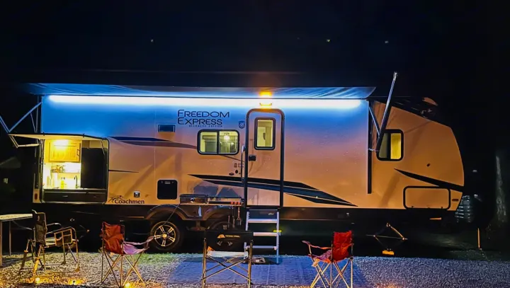 Illuminated rv rental with extended awning, outdoor kitchen, and chairs at a cozy night campsite.. Forest River Coachmen Freedom Express 2025
