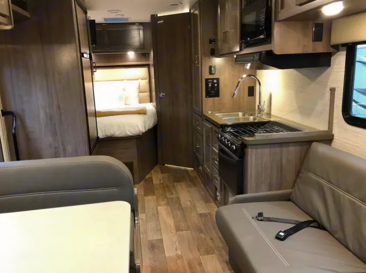 A modern rv rental interior showcasing a compact kitchen, bedroom, and living space with wood-look finishes.. Winnebago Minnie Winnie 2023