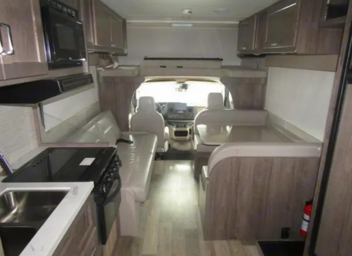 Interior of an RV rental features a kitchen, dinette, and the front cab with an overhead sleeping area.. Winnebago Minnie Winnie 2023