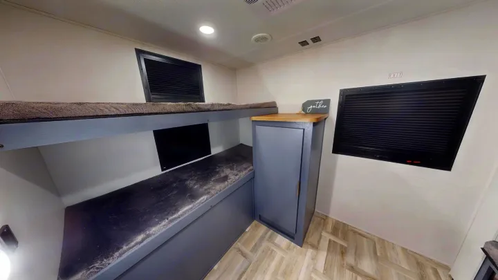 This RV rental interior shows two grey bunk beds, a storage cabinet, and windows with blinds, ideal for a comfortable stay.. Prime Time Tracer 2025