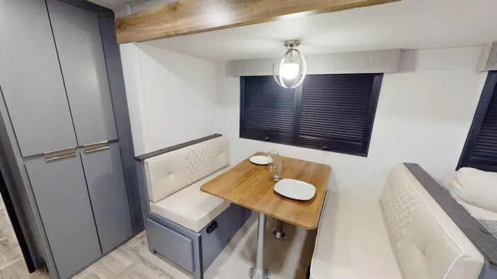 Well-appointed RV rental interior: a modern dinette with cozy cushioned benches, a wooden table, and gray storage cabinets.. Prime Time Tracer 2025