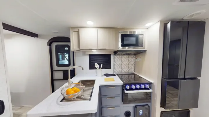 Modern RV rental kitchen featuring a sink, stove, microwave, and fridge. Compact interior design optimized for travel.. Prime Time Tracer 2025