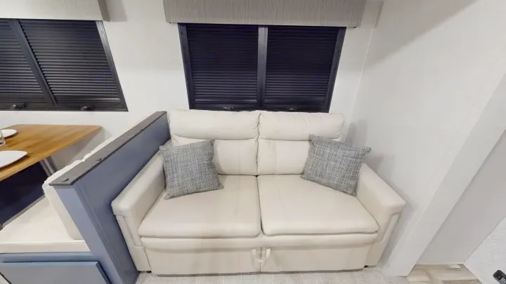Comfortable RV rental interior featuring a cream sofa with throw pillows, dual windows with blinds, and a dinette.. Prime Time Tracer 2025