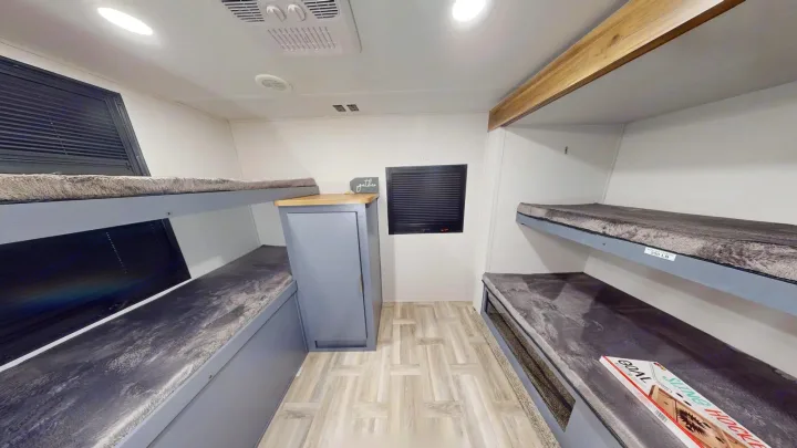 An RV rental bunk room features four cozy beds with grey plush cushions, a central storage cabinet, and natural light from windows.. Prime Time Tracer 2025