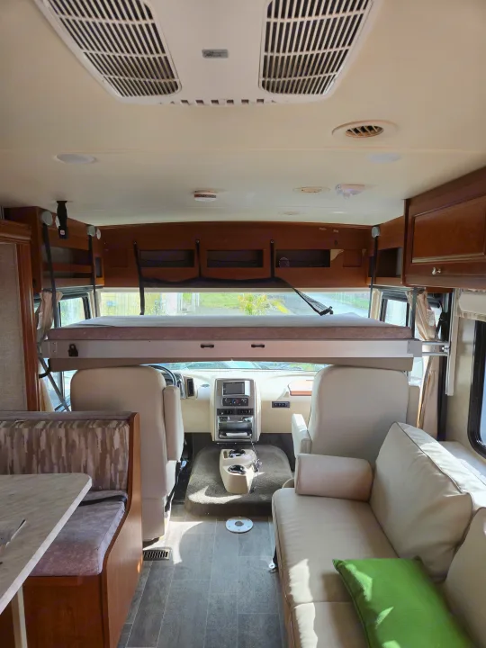 Spacious rv rental interior featuring an overhead bunk bed, cockpit, dining booth, and comfortable sofa.. Winnebago Sunstar 2019