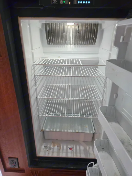 Empty Norcold RV refrigerator, showing some grime on shelves and walls, typical of an rv rental needing cleanup.. Winnebago Sunstar 2019