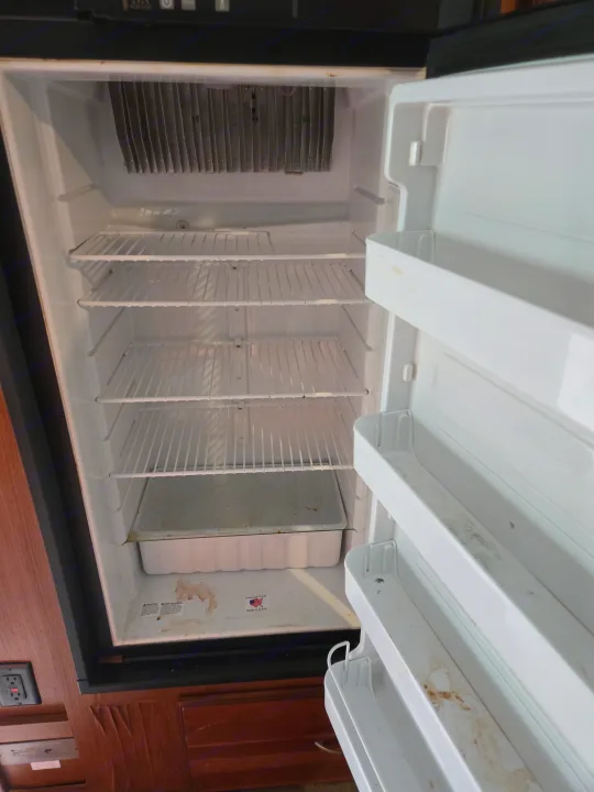Inside an empty, dirty RV rental refrigerator. Wire shelves & door bins are stained, showing it needs a deep clean.. Winnebago Sunstar 2019