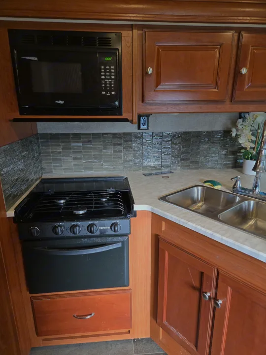 Full view of an RV rental kitchen showing a microwave, gas stove, double sink, and tiled backsplash.. Winnebago Sunstar 2019