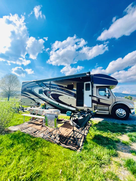 RV rental setup: A spacious RV parked on grass with awning extended, picnic table, and chairs under a blue, cloudy sky.. Jayco Seneca 2013
