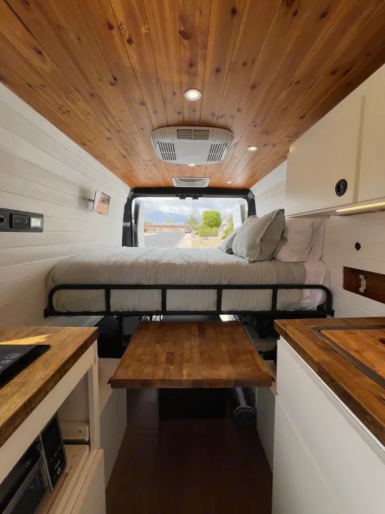 Spacious RV rental interior with custom wood ceiling, comfortable bed, kitchenette, and pull-out dining table. Ideal for travel.. Dodge Ram Promaster 2500 2022