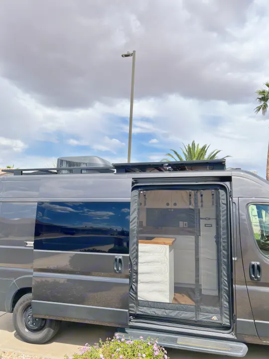 Dark grey camper van, an ideal RV rental, with its side door open showing a modern interior and rooftop AC/solar panels.. Dodge Ram Promaster 2500 2022