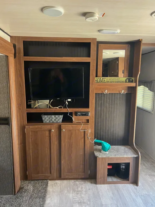 Step inside this RV rental showcasing a built-in entertainment & storage unit with TV, stereo, and coat rack, optimizing living space.. Heartland RVs Pioneer 2018