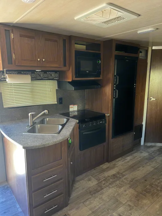 Modern RV rental kitchen with wood cabinets, double sink, stove, microwave, and fridge. Ready for your travels!. Heartland RVs Pioneer 2018