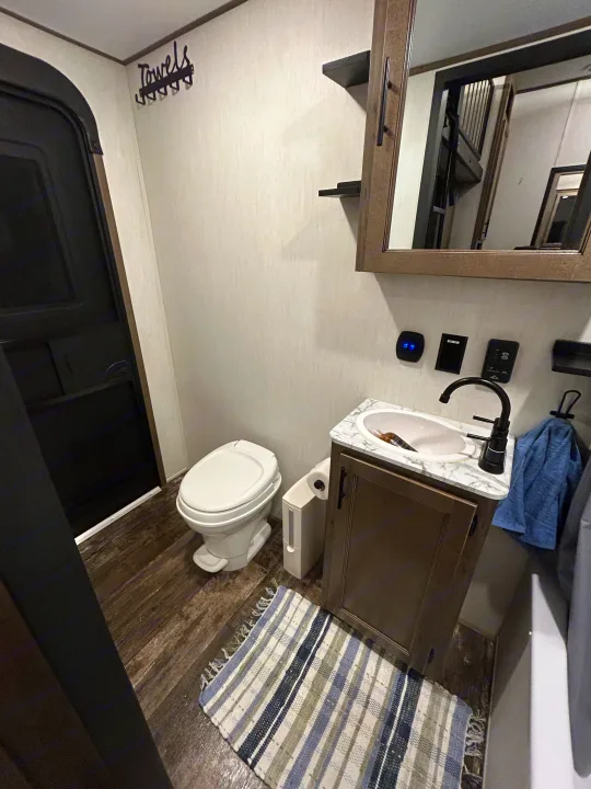 Inside an RV rental bathroom: functional space with vanity, sink, toilet, and mirror reflecting a staircase.. Forest River Sabre 2022