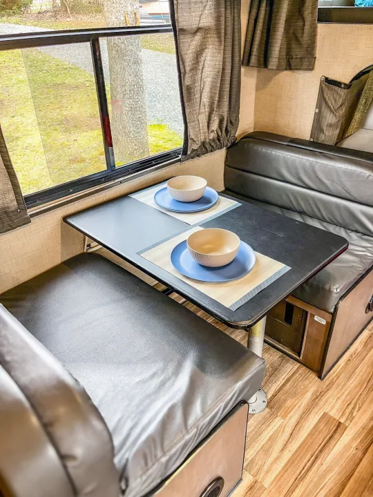 Inside an RV rental: a comfortable dinette with black faux-leather seats, a table set for two, and a window view.. Thor Majestic 2019