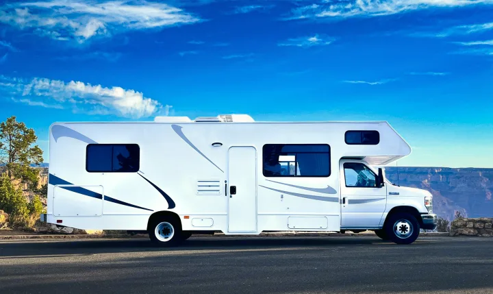 White RV rental parked at a Grand Canyon overlook with a bright blue sky & clouds. Ideal for scenic travel.. Thor Majestic 2019