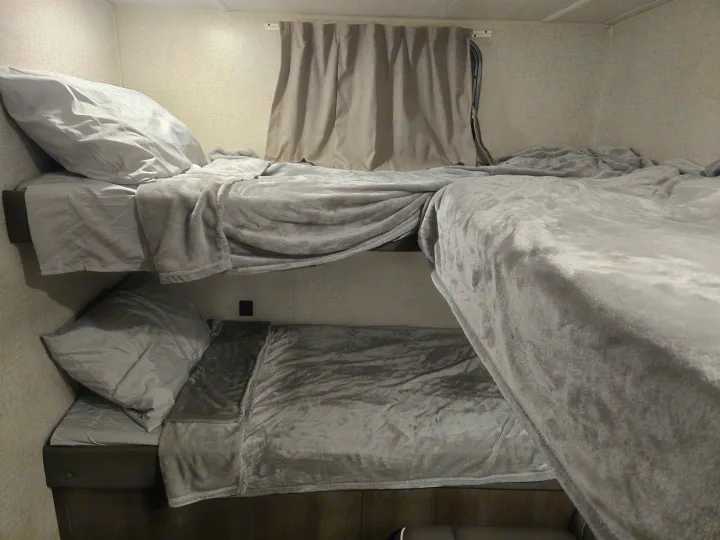 Cozy grey bunk beds in this RV rental offer comfortable sleeping for travel. Features soft bedding, window, and power outlet.. Forest River Salem Cruise Lite 2021