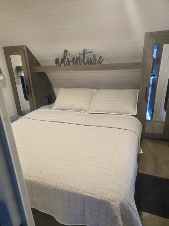 Comfortable RV rental bedroom featuring a clean bed, overhead shelf with an "adventure" sign, and bedside mirrors.. Forest River Salem Cruise Lite 2021