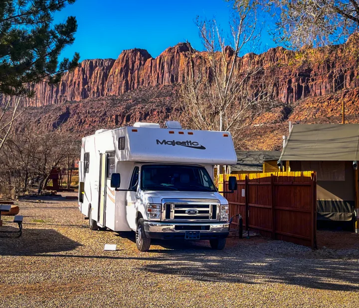 Majestic rv rental at a sunny campsite, framed by impressive red rock mountains and blue skies. Ideal for a scenic outdoor adventure.. Thor Majestic 2019
