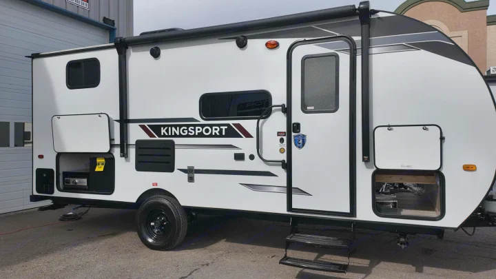 Exterior side view of a white Kingsport travel trailer, ideal for your next RV rental adventure. Features an open storage hatch and entrance steps.. Gulf Stream Kingsport 192DS 2025