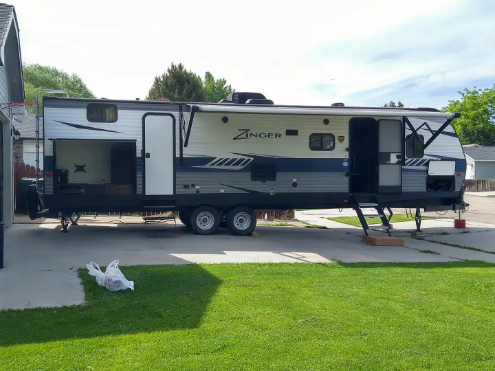 Zinger RV rental parked on a driveway, its extended side revealing an outdoor kitchen.. Crossroads RV Zinger 2020
