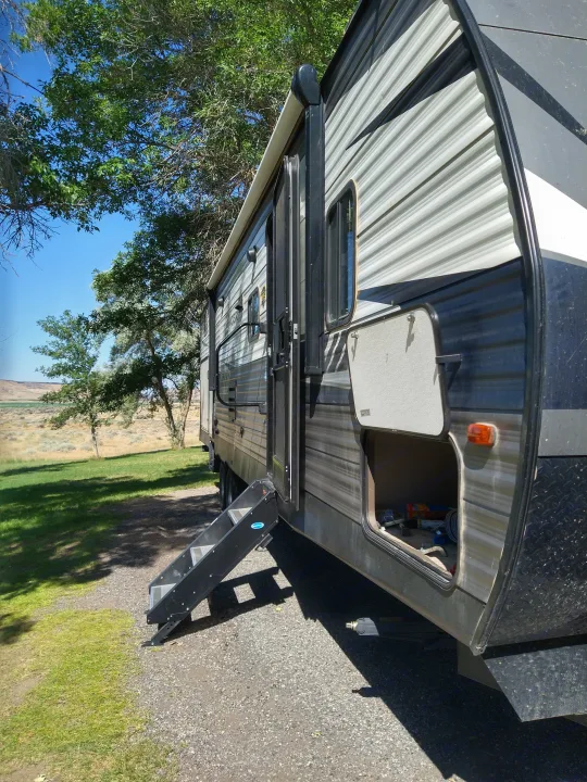 Side view of an RV rental with open door, extended steps, and a storage compartment, parked in a scenic outdoor setting.. Crossroads RV Zinger 2020
