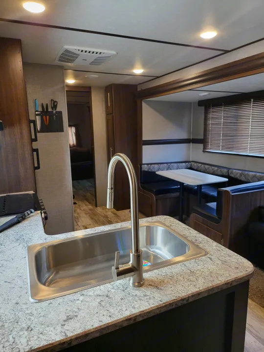 Bright RV rental interior showcasing a well-equipped kitchen with a large sink and a cozy U-shaped dinette area.. Crossroads RV Zinger 2020