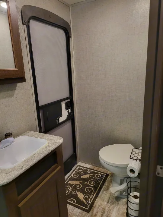 This RV rental bathroom features a sink on a light counter, a toilet with a wire TP holder, and a decorative floor mat.. Crossroads RV Zinger 2020