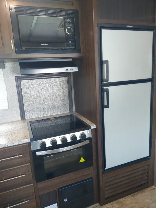 RV rental kitchen showing a modern interior with Greystone microwave/stove/oven and Dometic refrigerator for comfortable travels.. Crossroads RV Zinger 2020