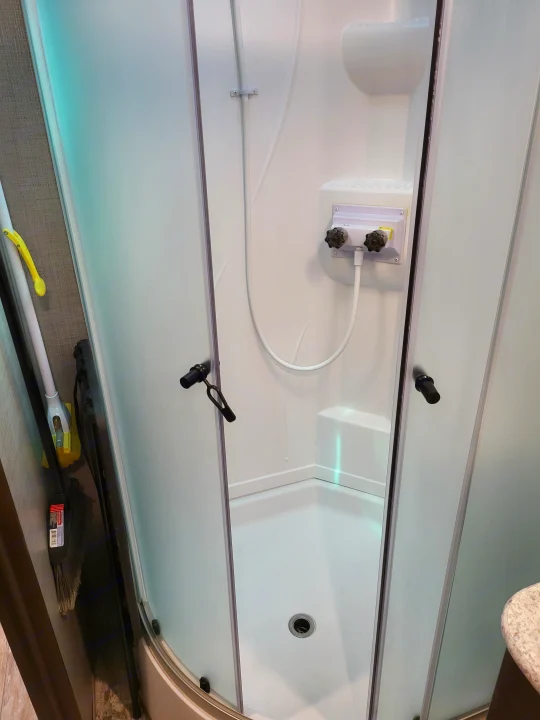 Inside an RV rental, a compact shower with frosted glass doors, controls, and a drain is visible.. Crossroads RV Zinger 2020