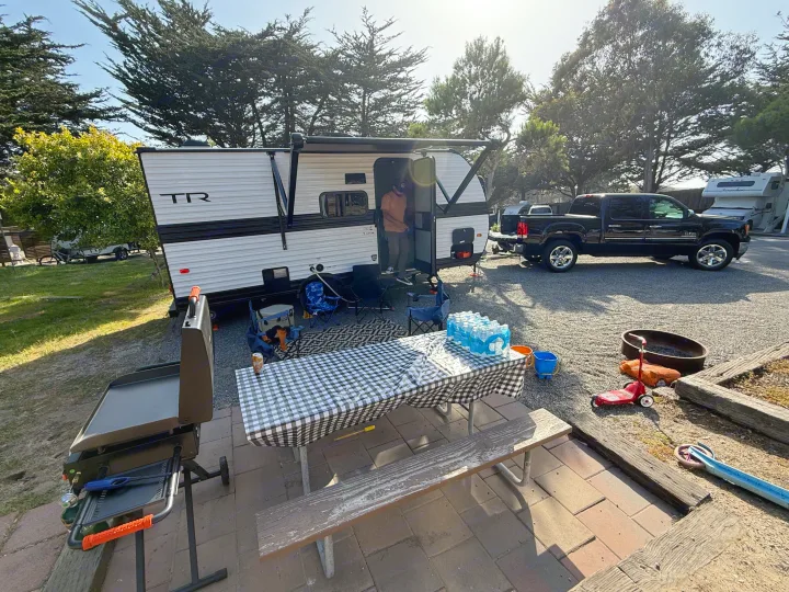 RV rental camper and truck parked at a sunny campsite. Features a picnic table, grill, and fire pit for outdoor fun.. Heartland Trail Runner 2025