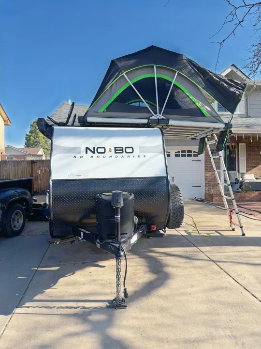 Experience outdoor adventure with this RV rental! A No Boundaries travel trailer with its rooftop tent and ladder set up.. No Boundaries 10 Toy Hauler 2022