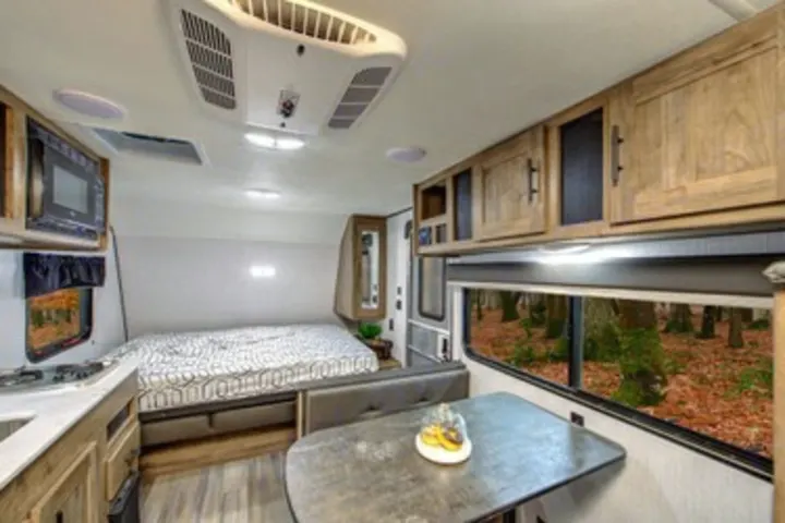 Inside a modern RV rental: a compact kitchen, comfortable bed, dinette, and fall forest views from the window.. Heartland RVs Pioneer 2022