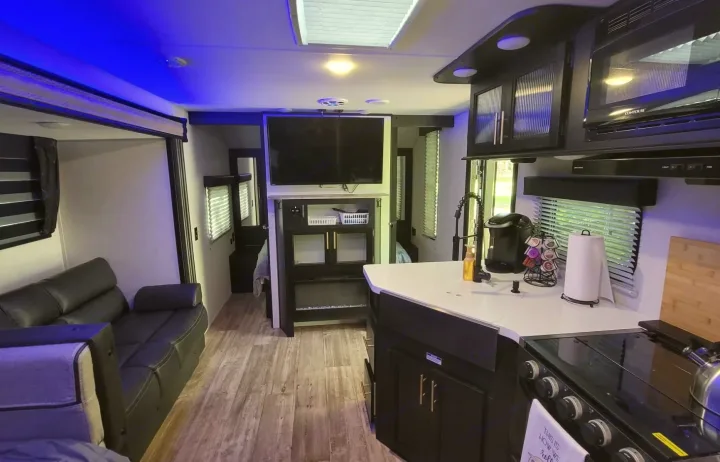 Spacious RV rental interior features a modern kitchen, living area with sofa & TV, and blue ambient lighting.. Forest River Cherokee Grey Wolf 2022