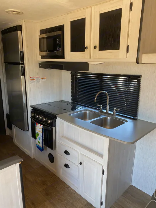 RV rental kitchen: stainless steel fridge, microwave, oven, and double sink. Light wood-look cabinets, window blinds.. Heartland Trail Runner 2021