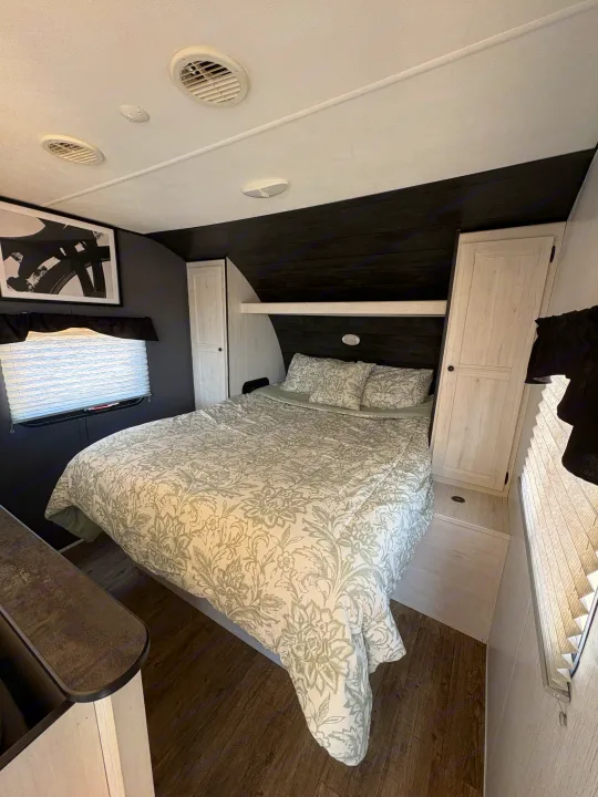 Modern RV rental bedroom interior features a patterned bed, black walls, and light wood cabinets. Functional and stylish.. Heartland Trail Runner 2021