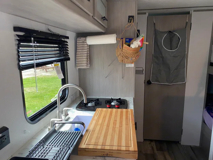 RV rental kitchen amenities: sink, stove, drying rack, and "Welcome Ellyn+family" basket in a compact camper.. Coleman Lantern 17B 2024