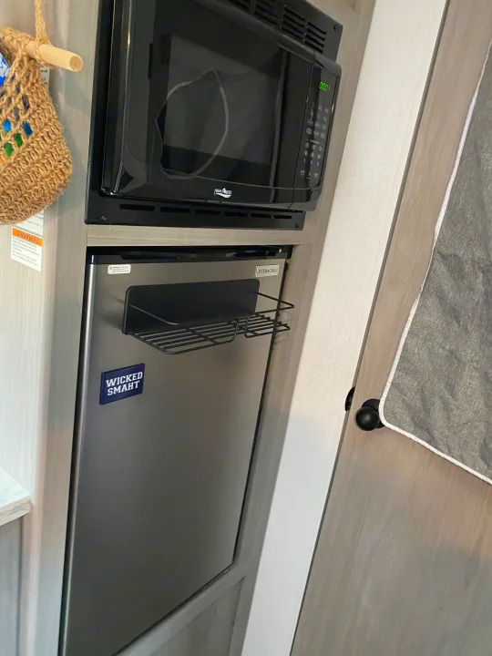 Compact kitchen in an RV rental, featuring a High Pointe microwave above an Ever&Chill mini-fridge with a "Wicked Smaht" magnet.. Coleman Lantern 17B 2024