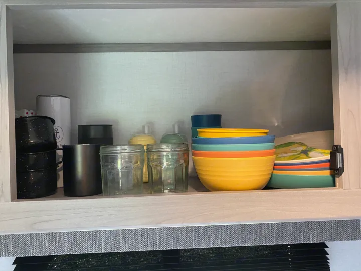 Inside an RV rental cabinet: colorful bowls, mugs, and clear glass jars, organized for compact kitchen storage.. Coleman Lantern 17B 2024