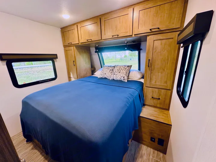 This comfortable RV rental bedroom features a blue bed, ample storage cabinets, and large windows for scenic views.. Forest River Coachmen Freedom Express 2025