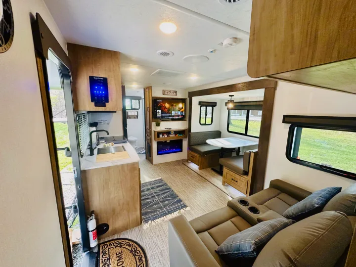 Modern rv rental interior: kitchen with control panel, dining nook, TV with fireplace, & reclining sofa with cup holders.. Forest River Coachmen Freedom Express 2025