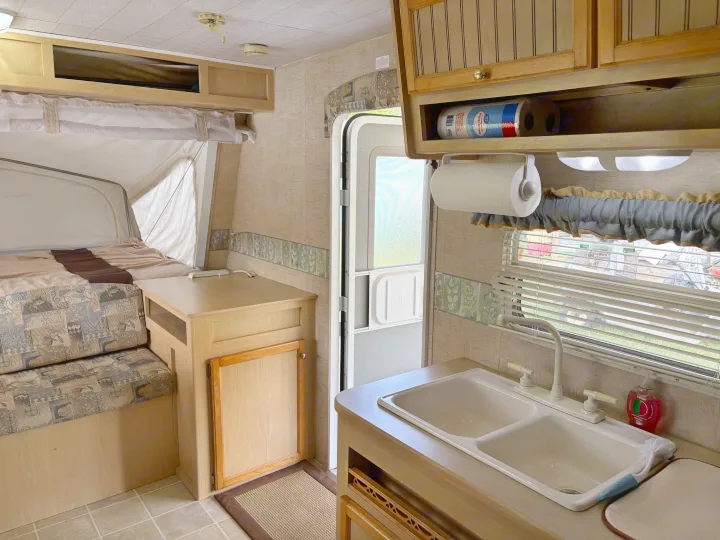RV rental interior: A cozy pop-up camper featuring a kitchen, dinette, and comfortable bed area.. Jayco Jay Feather EXP 2005